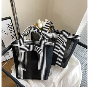 Detail of black mesh tote bag with striped handles and a large decorative bow