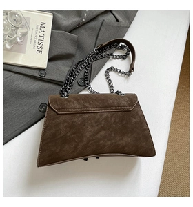 Macro detail of dark brown matte leather bag with metallic chain strap on a white table