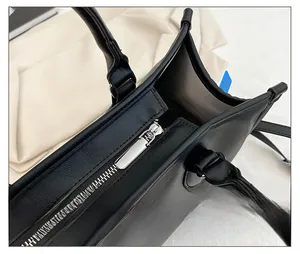 Close-up of the smooth silver zipper and leather texture on a black tote bag