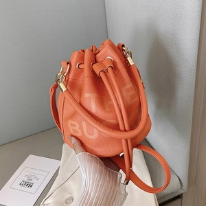 Detail of orange drawstring bucket bag with litchi texture and THE BUCKET lettering