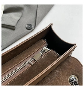 Detail of brown leather square bag showing silver zipper and metallic chain strap