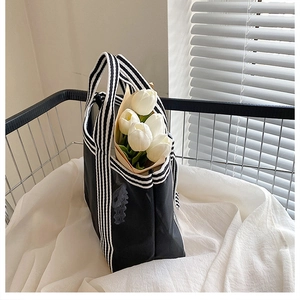 Detail of a minimalist tote bag with black and white striped handles and white tulips