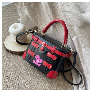 Detail of box handbag featuring a cartoon rabbit, red handle, and golden metal studs