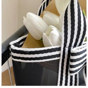 Detail of minimalist black mesh tote bag featuring striped webbing handles and flowers