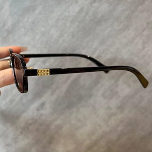 Close-up of black square sunglasses featuring gold square stud accents on the temples