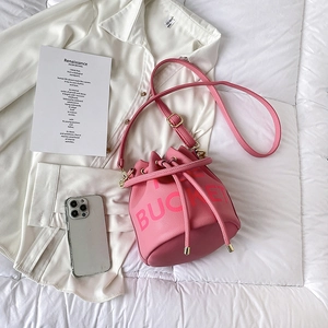 Flat lay of pink drawstring bucket bag with litchi texture and gold hardware accents