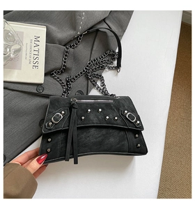 Detail of black rivet handbag with chain strap and tassels on a grey blazer