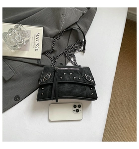 Detail of black punk style crossbody bag with silver rivets and metal chain strap