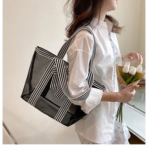 Detail of black mesh tote bag with striped canvas strap shown with white floral dress