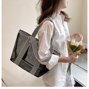 Detailed shot of large black mesh tote bag with striped canvas strap for beach use