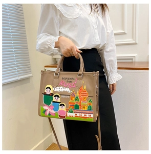 Macro view of khaki leather tote bag featuring colorful Russian doll embroidery and sturdy handles