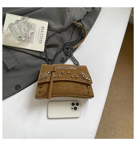 Close-up of brown studded leather crossbody bag with chain strap next to a smartphone