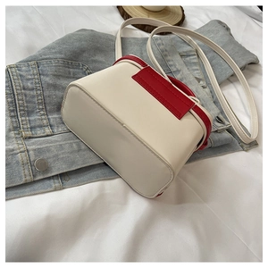 Detail view of contrast color box bag with cream leather and red handle on denim