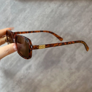 Close-up of tortoise shell square frame sunglasses with gold pyramid rivet detail
