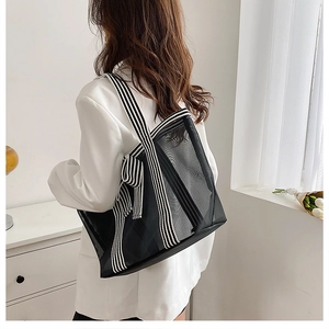 Detail of large black mesh tote bag with striped shoulder strap shown on a model