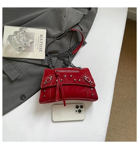 Detail of red leather crossbody bag with punk rivets and metal chain on modern background