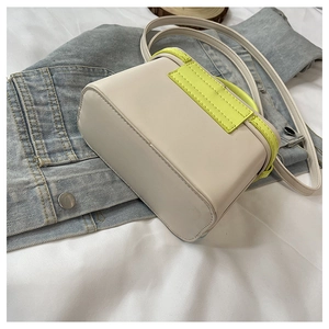 Top view of a cream box-shaped handbag with neon green accents on denim fabric