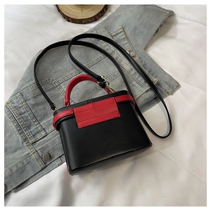 Detail view of red and black contrast mini crossbody bag with golden hardware on denim