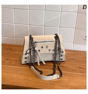 Close-up of beige punk style crossbody bag with black rivets and heavy metal chain strap