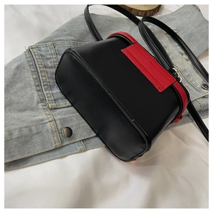 Detail of black leather crossbody bag with red contrast stitching on blue denim fabric