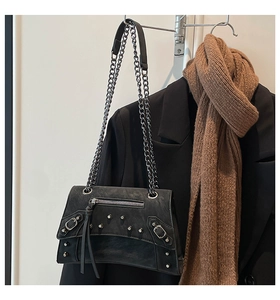 Close-up of black punk rivet crossbody bag with silver chains on a blazer background