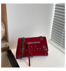 Detail of red leather crossbody bag with silver studs and decorative tassels on desk