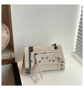 Detail of rivet decor and long tassel zipper on a cream motorcycle chain bag