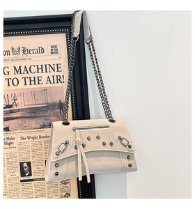 Close-up of beige leather crossbody bag with rivet studs and dark metal chain detail