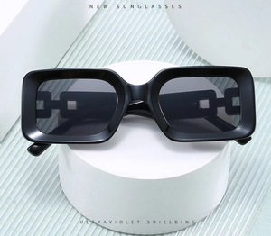 Detail of black rectangular sunglasses with hollow chain link temples on a white pedestal