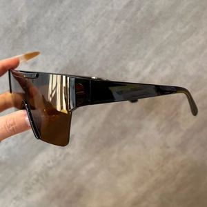 Détail de lunettes de soleil shield avec larges branches noires et verres marron