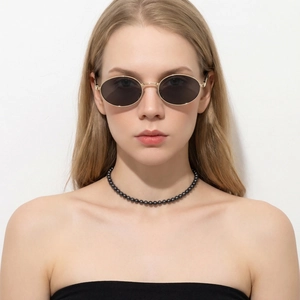 Détail de lunettes de soleil ovales en métal et collier de perles noires sur un mannequin