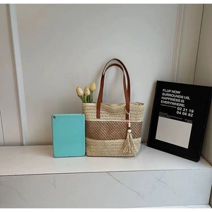 Detail of color-block woven straw tote with leather handles and tassel accent