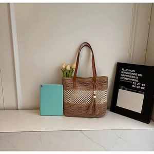Detail of striped straw tote bag featuring brown leather straps and stylish tassel charm
