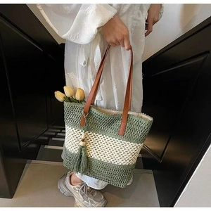 Detail of striped straw bag featuring green tassels and brown leather shoulder strap