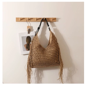 Detail of hollow woven straw tote bag featuring long fringes and black leather handle