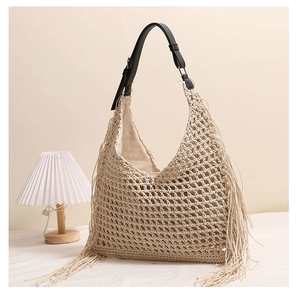 Detail of bohemian woven straw bag featuring decorative long tassels and black leather strap