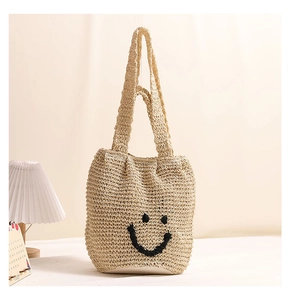 Detail of handwoven straw tote bag featuring a black embroidered smiley face design