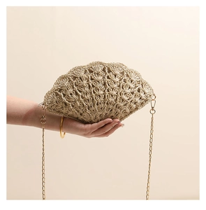 Macro detail of hand-held straw shell bag with woven hollow texture and gold chain strap