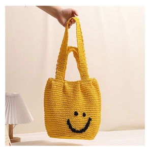 Close-up of yellow woven tote bag with a black smiley face embroidery and soft dual handles