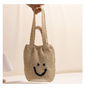 Detail of beige woven straw tote bag featuring a black embroidered smiley face design