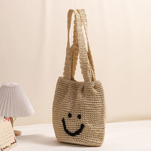 Handwoven straw tote bag with a black smiley face embroidery for summer beach vacations