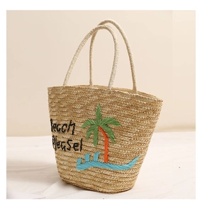 Dettaglio del ricamo a palma e scritta Beach Please sulla borsa in paglia