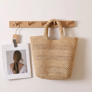 Hollow-out beige raffia straw tote bag for beach vacations hung on a wooden hook