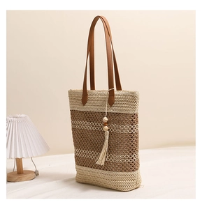 Detailaufnahme der Strohtasche mit Quastenanhänger und braunen Ledergriffen
