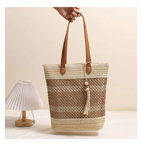 Detail einer handgehaltenen gestreiften Strohtasche mit Ledergriffen und Quasten