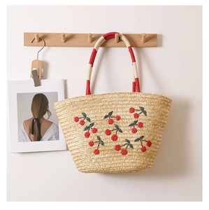 Detailed view of cherry embroidery on straw tote bag with red striped handles