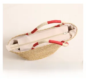 Detail view of woven straw beach bag featuring a red rope handle and smooth zipper closure