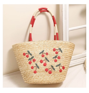 Close-up of cherry embroidery details and red woven handles on straw beach tote bag