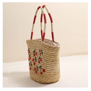 Detail of red cherry embroidery and dual-tone woven handles on summer straw tote bag