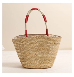 Detail of hand-woven straw bag featuring red and white striped handles and embroidery